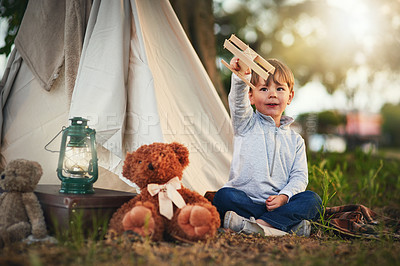 Buy stock photo Shot of a cute little boy playing with a toy airplane while sitting outside his teepee