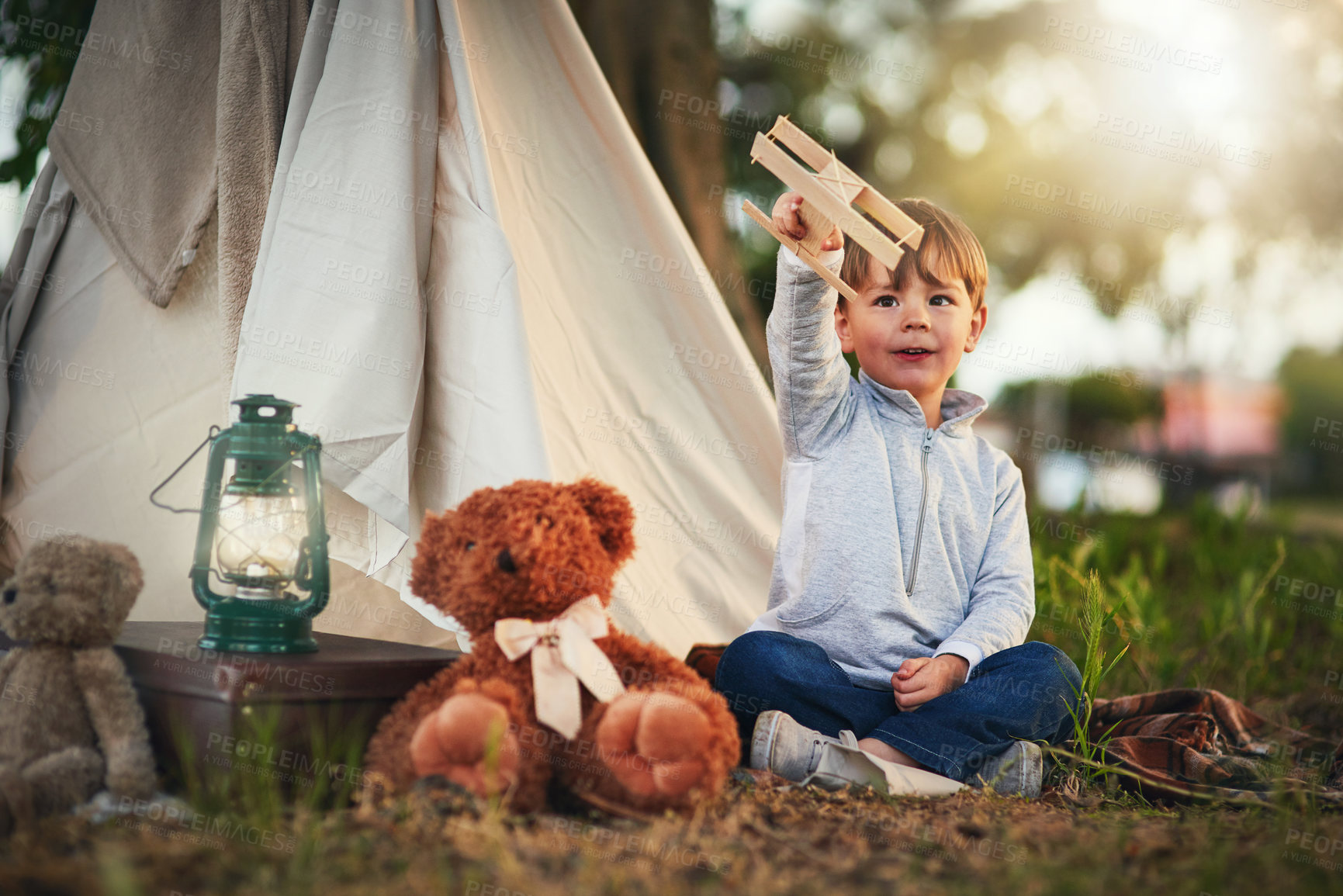 Buy stock photo Shot of a cute little boy playing with a toy airplane while sitting outside his teepee