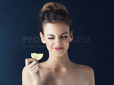Buy stock photo Cropped shot of a beautiful young woman eating a slice of lemon against a dark background