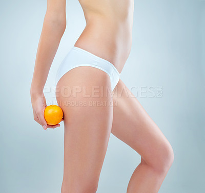 Buy stock photo Shot of an unidentifiable young woman posing in her underwear while holding an orange in studio