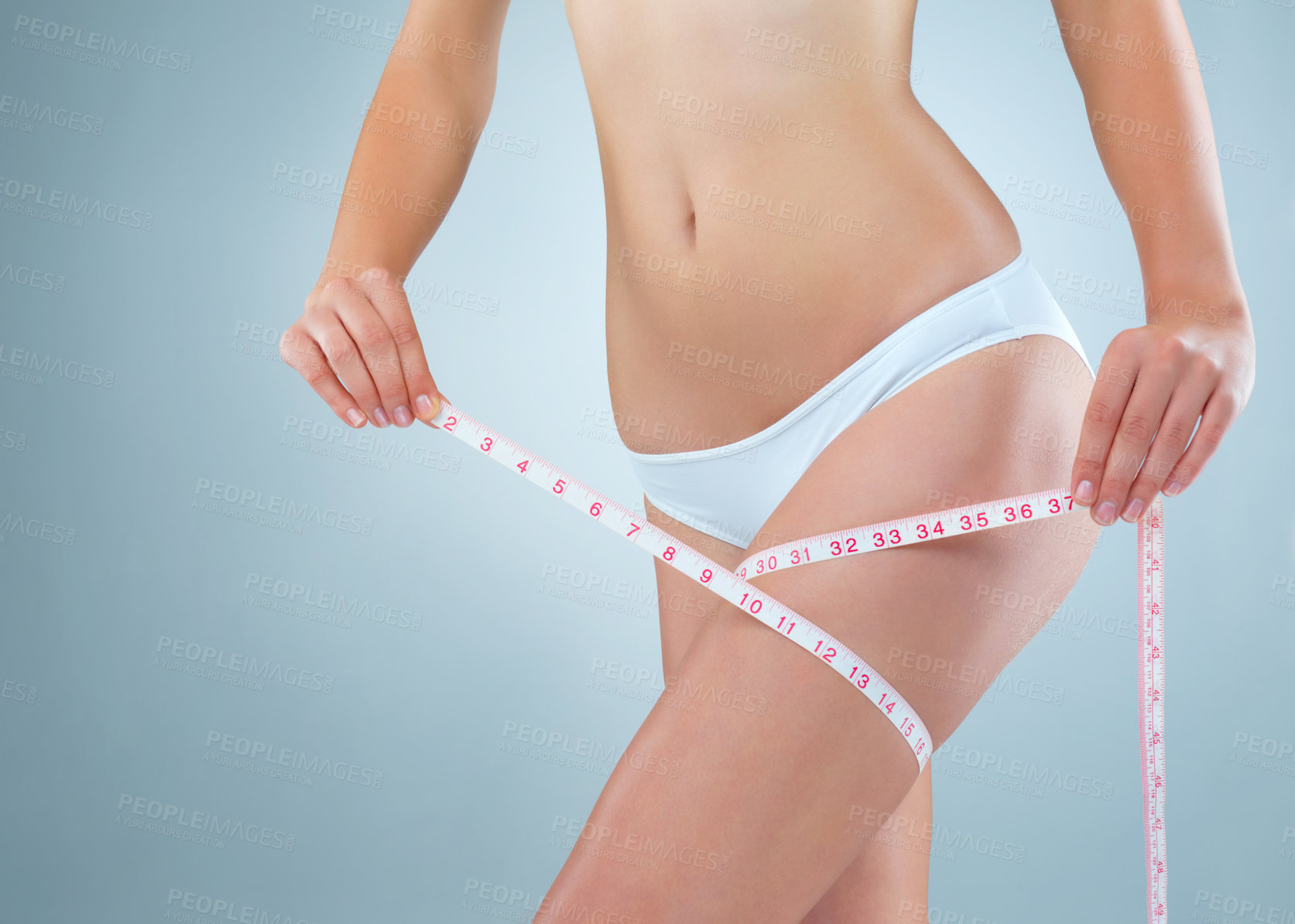 Buy stock photo Shot of an unidentifiable young woman using a measuring tape to measure her thigh in studio