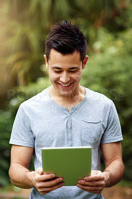 Buy stock photo Shot of a handsome young man using a digital tablet outside