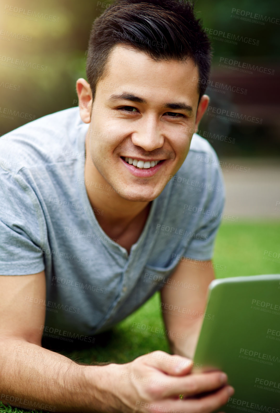 Buy stock photo Portrait of a handsome young man using a digital tablet while lying on the grass outside