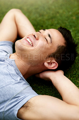 Buy stock photo Shot of a handsome young man relaxing on the grass outdoors