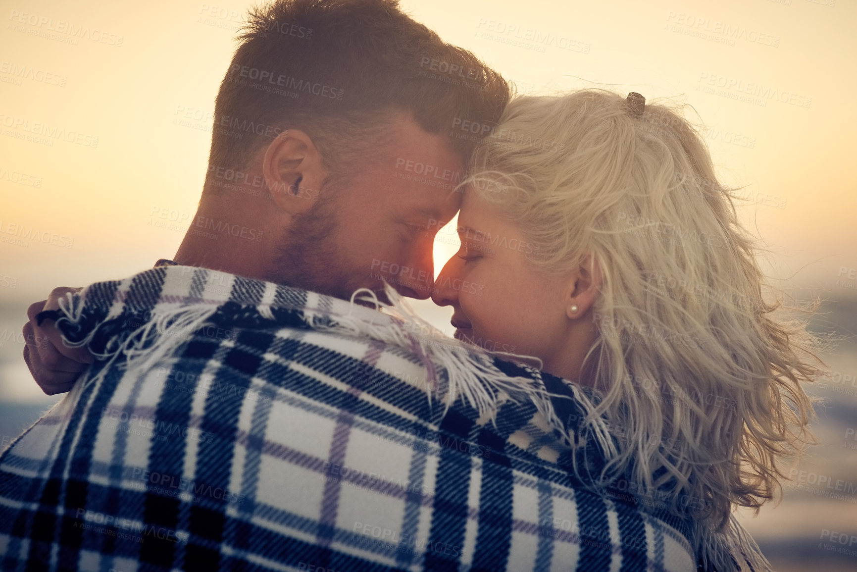 Buy stock photo Couple, hug and love at beach, sunset and eyes closed for connection, bonding or relax with blanket, Man, woman and partner with embrace for smile, care or happy memory on vacation by sea in sunshine