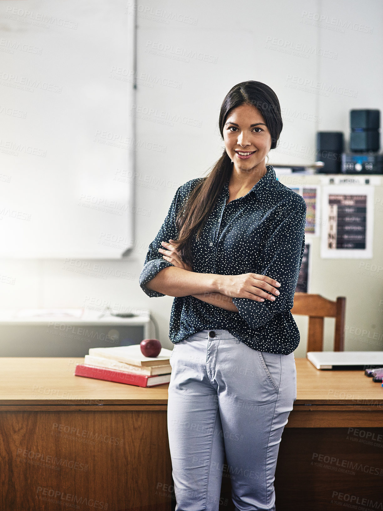 Buy stock photo Portrait of an attractive young teacher standing with her arms folded in a classroom