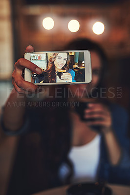 Buy stock photo Shot of a happy young woman using her smartphone to take a selfie in a coffee shop