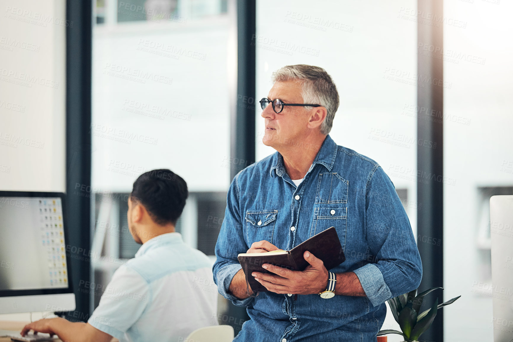 Buy stock photo Shot of a creative entrepreneur making notes in his notebook while standing in the office