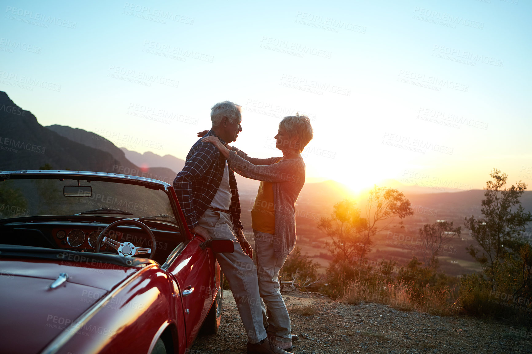 Buy stock photo Shot of an affectionate senior couple enjoying the sunset during a roadtrip