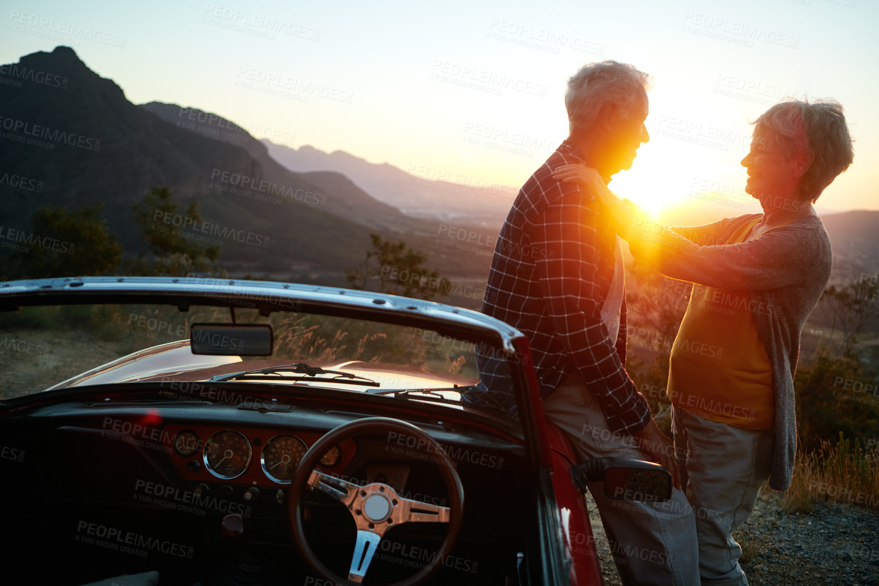 Buy stock photo Shot of an affectionate senior couple enjoying the sunset during a roadtrip