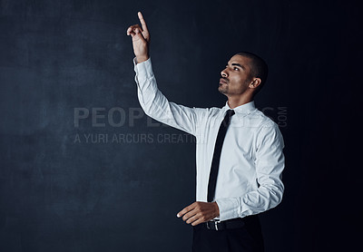 Buy stock photo Studio shot of a young businessman connecting to a user interface with his finger against a dark background