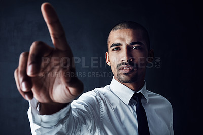 Buy stock photo Studio shot of a young businessman connecting to a user interface with his finger against a dark background