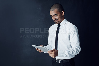 Buy stock photo Studio shot of a young businessman using a digital tablet against a dark background