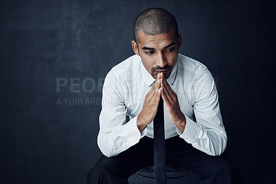 Buy stock photo Studio shot of a young businessman looking thoughtful against a dark background