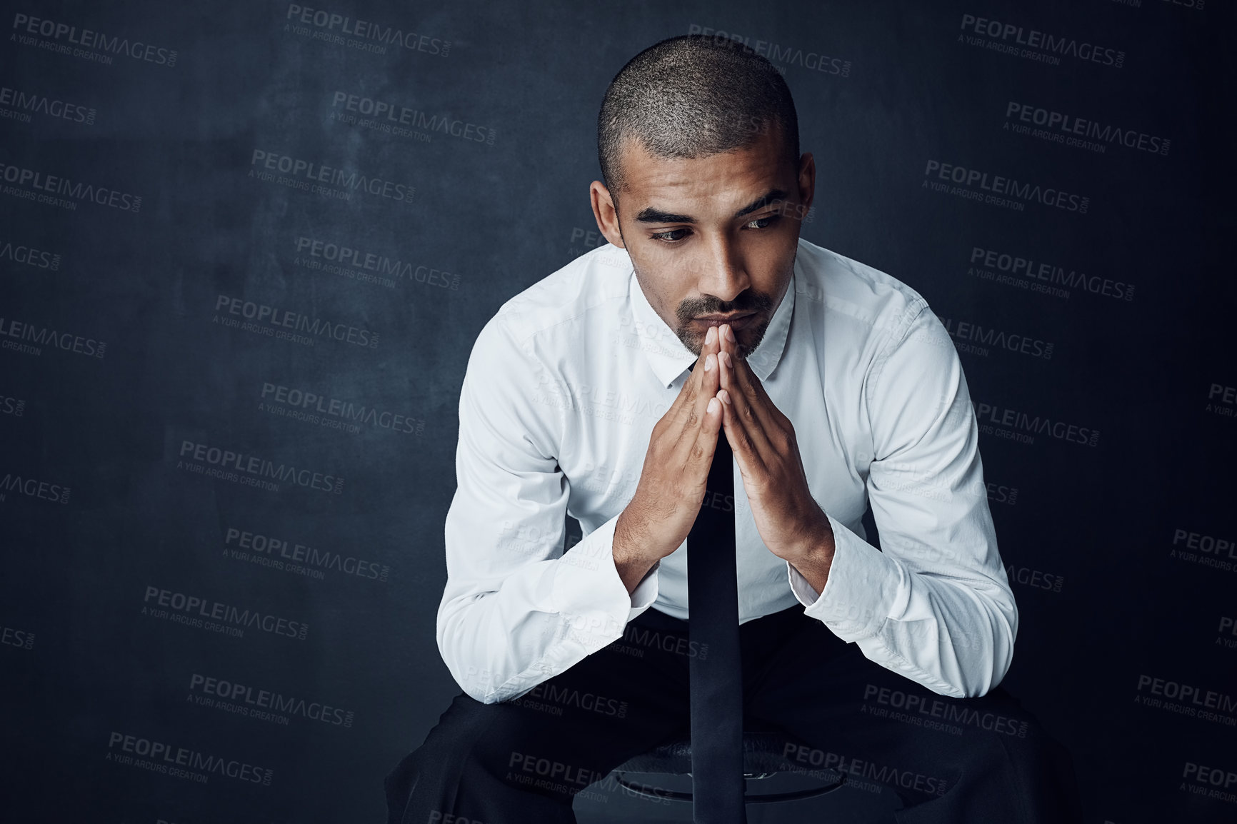 Buy stock photo Studio shot of a young businessman looking thoughtful against a dark background