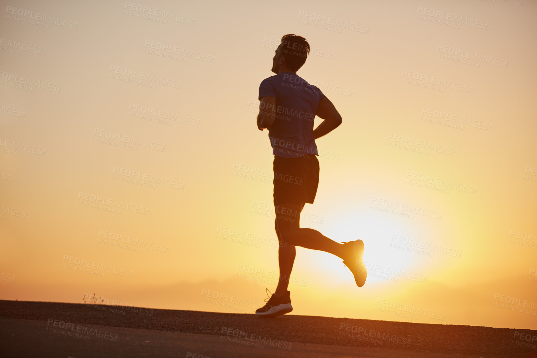 Buy stock photo Shot of a silhouetted young man out for a run at sunrise