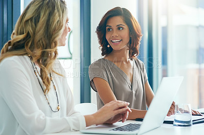 Buy stock photo Shot of two businesswomen having a discussion while using a laptop