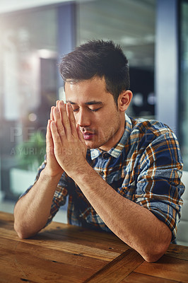 Buy stock photo Shot of a young designer sitting in an office with his hands clasped in prayer