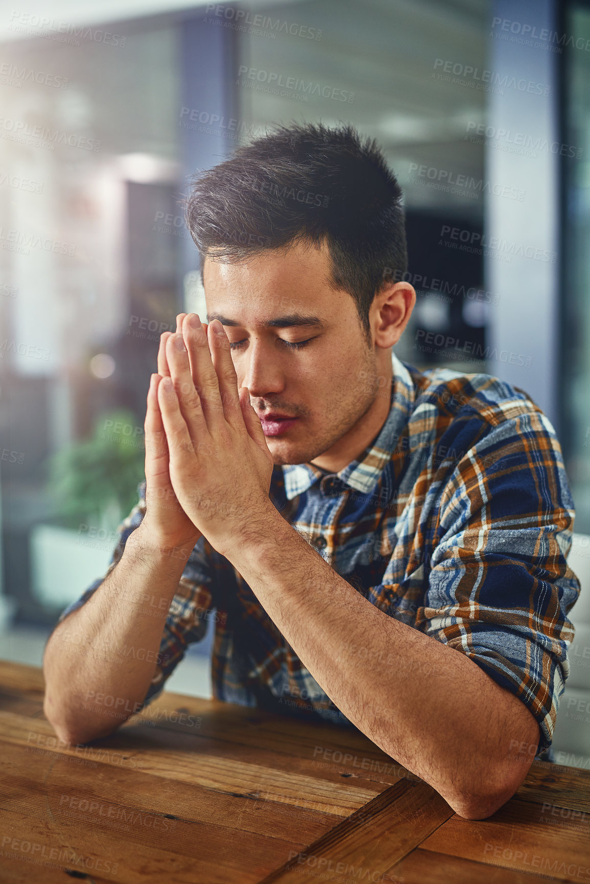 Buy stock photo Shot of a young designer sitting in an office with his hands clasped in prayer