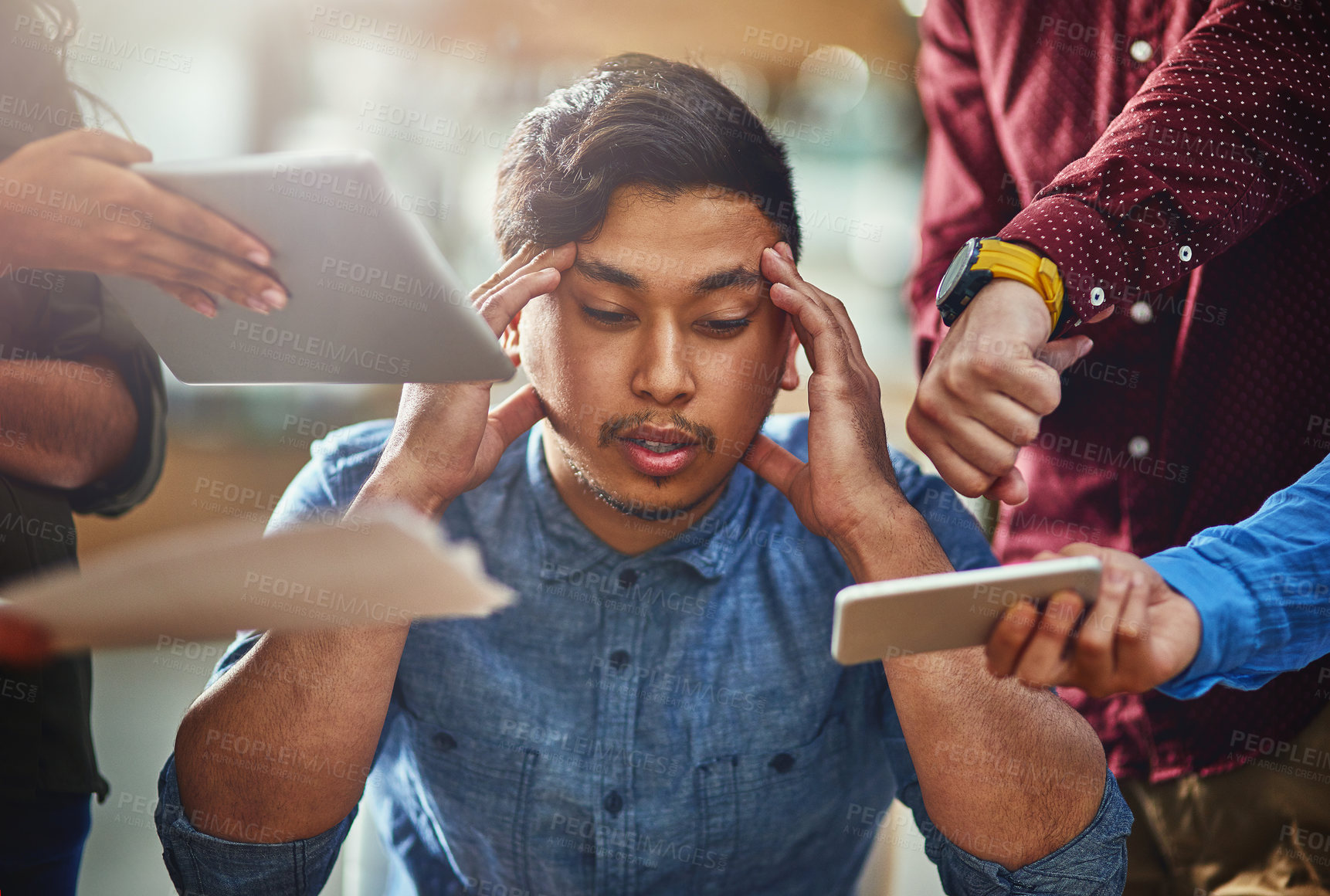 Buy stock photo Shot of a stressed out designer surrounded by demanding colleagues while sitting at his office desk