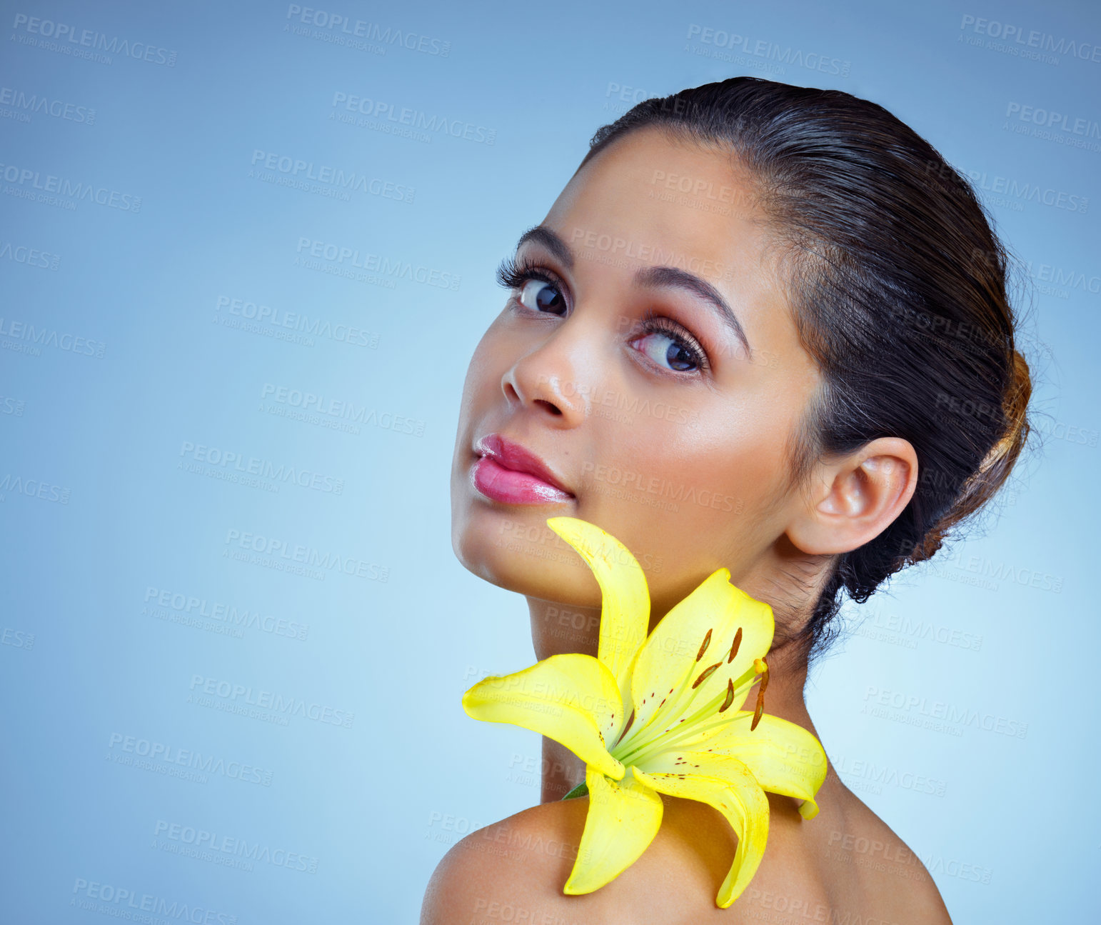 Buy stock photo Studio portrait of a beautiful young woman posing with a flower against a blue background