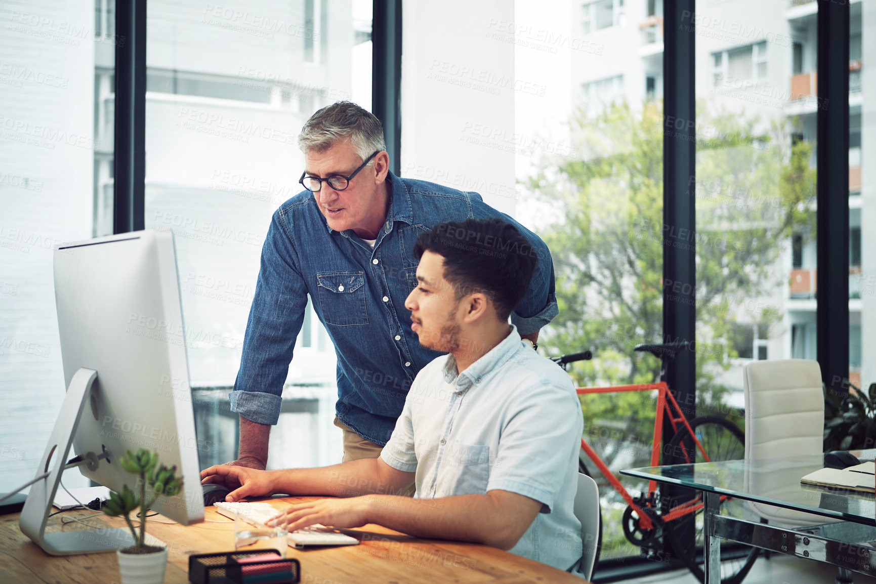 Buy stock photo Shot of a mature designer helping a younger colleague with some designs