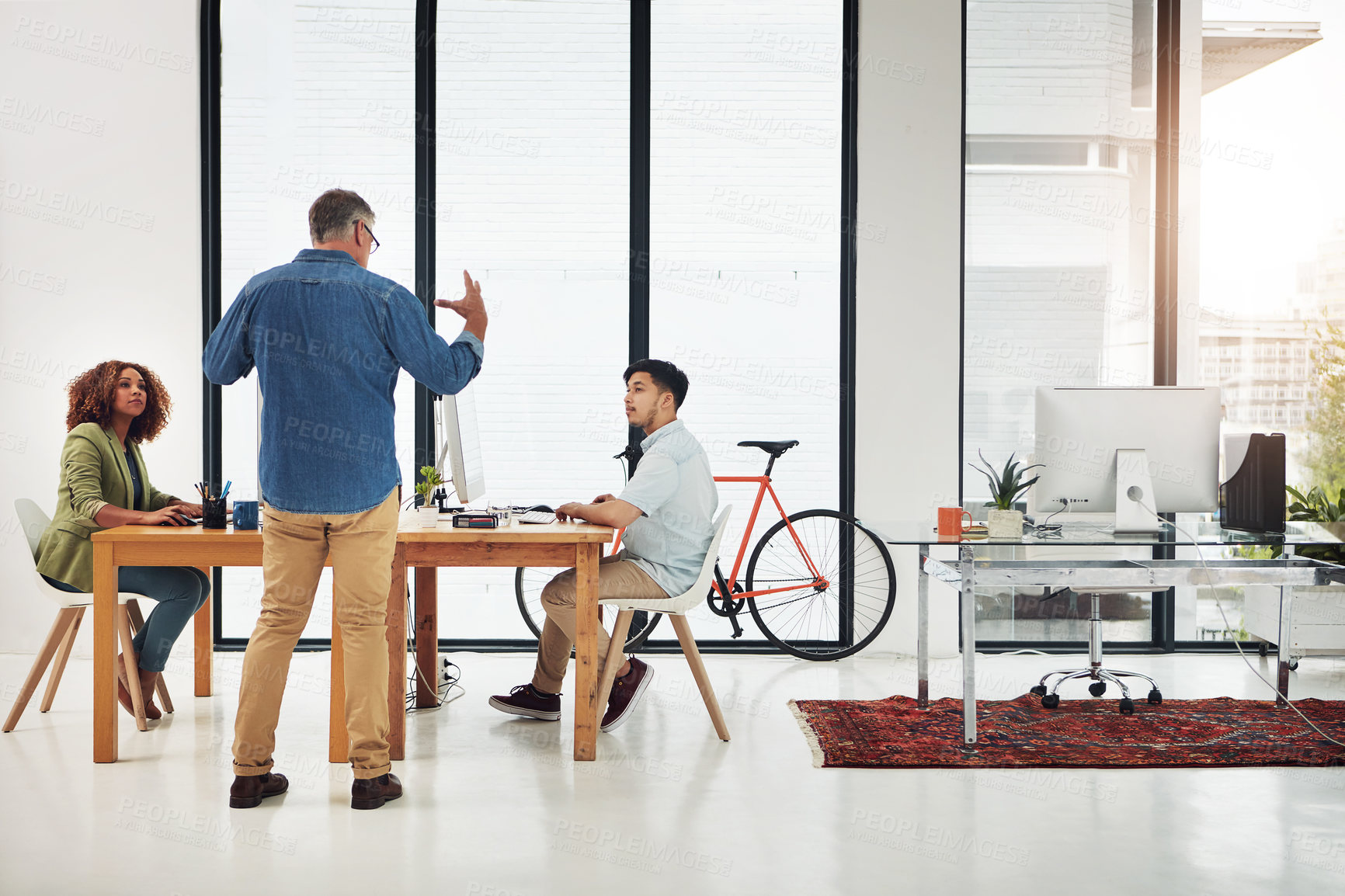 Buy stock photo Shot of a mature businessman addressing two employees in the office