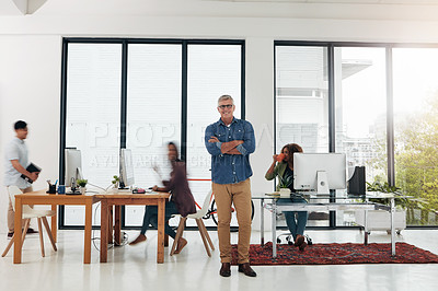 Buy stock photo Portrait of a mature designer standing in the office with his colleagues in the background