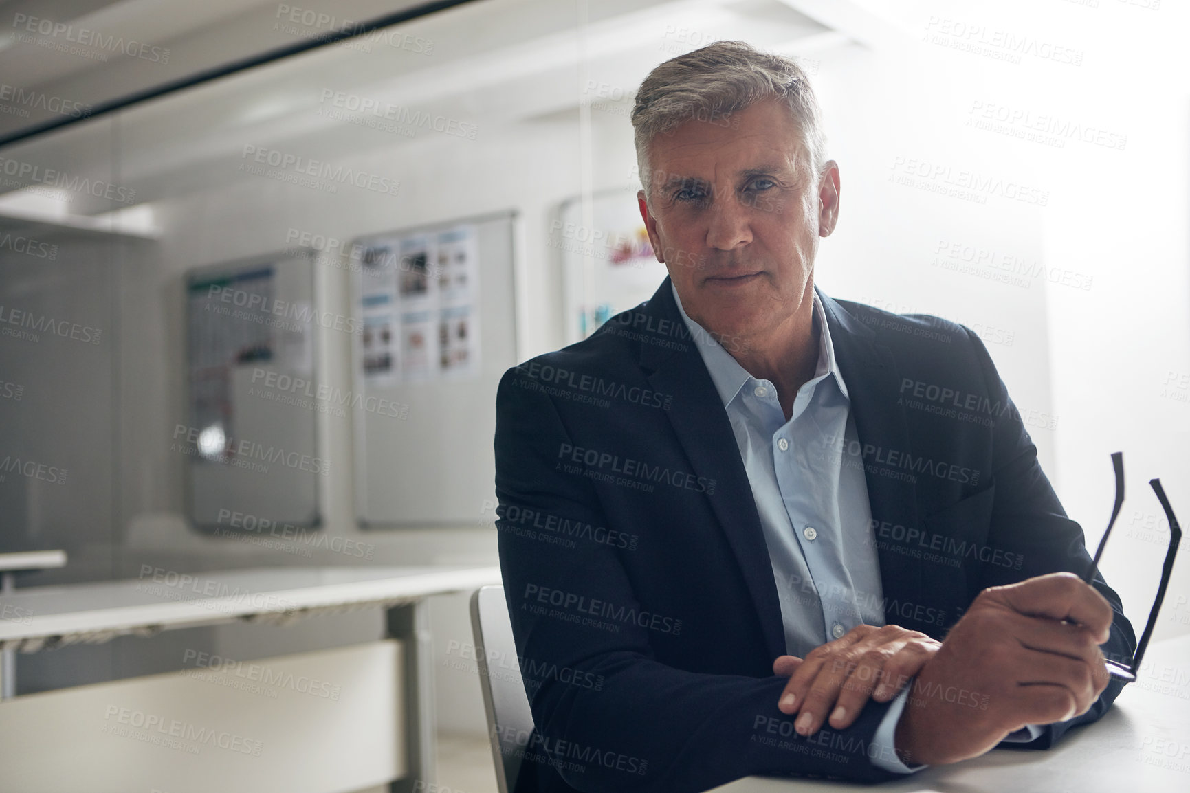 Buy stock photo Portrait of a confident businessman holding his glasses while sitting at a desk in the office