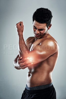 Buy stock photo Cropped shot of a sporty young man holding his elbow in pain against a grey background