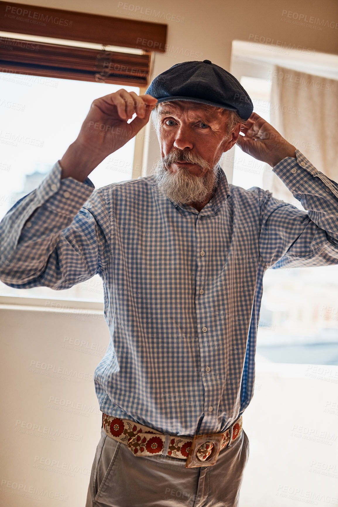 Buy stock photo Portrait of a cheerful senior man trying on one of his hats while looking at the camera