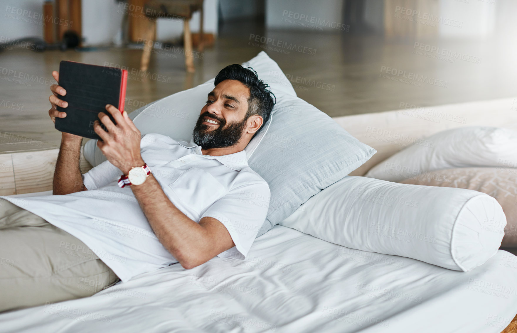 Buy stock photo Shot of a easygoing bachelor using his tablet while relaxing on the couch at home