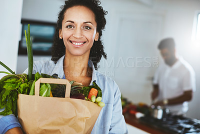 Buy stock photo Portrait of a happy woman holding a bag of fresh vegetables while standing in her kitchen