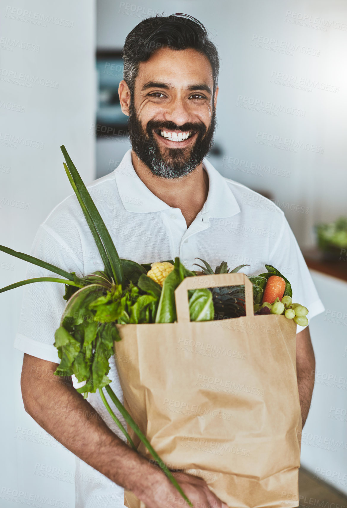 Buy stock photo Portrait of a happy man holding a bag of fresh vegetables while standing in his kitchen