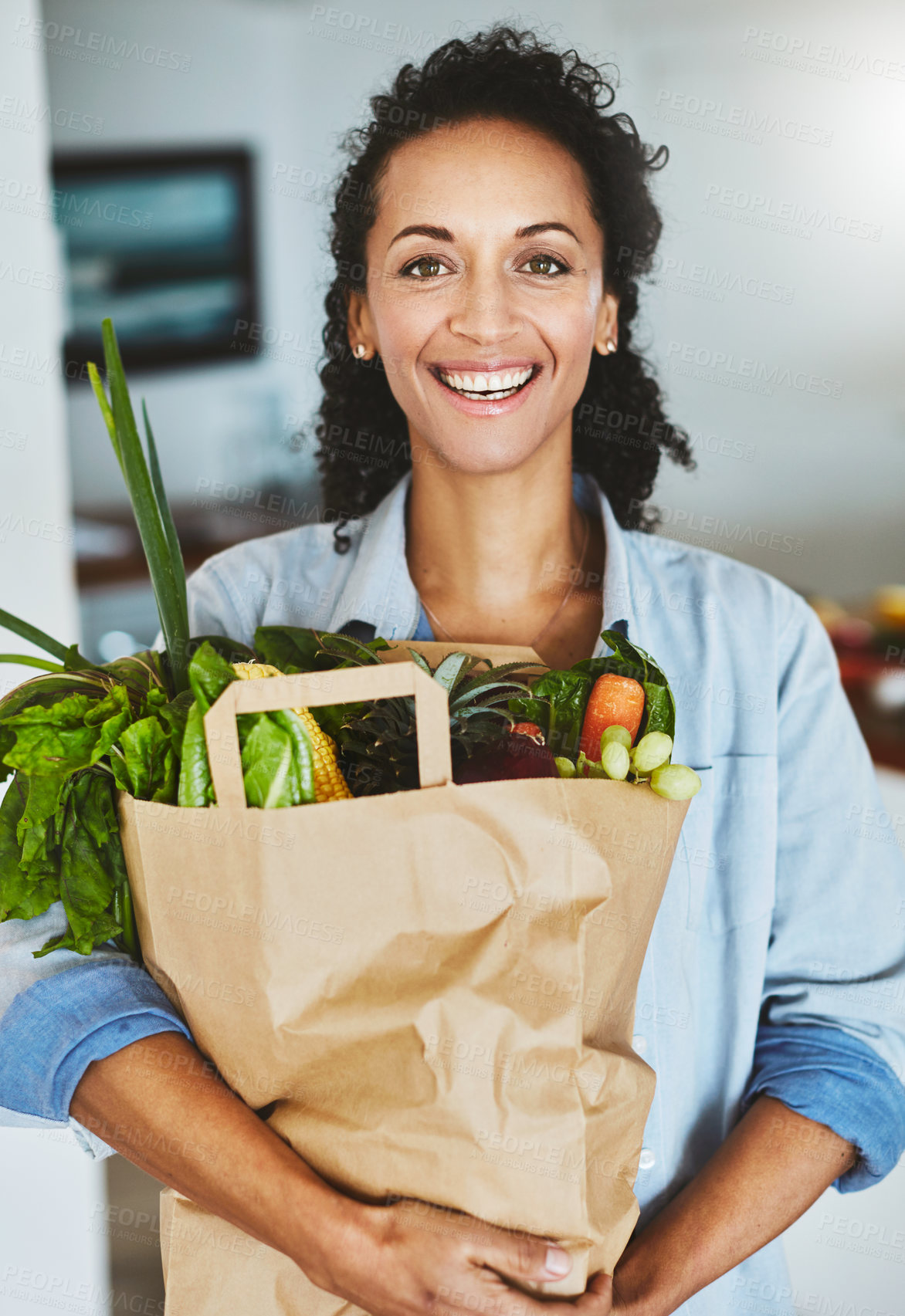 Buy stock photo Portrait of a happy woman holding a bag of fresh vegetables while standing in her kitchen