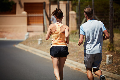 Buy stock photo Rearview shot of an unidentifiable couple jogging together in their neighborhood