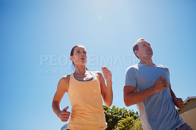 Buy stock photo Low angle shot of a happy couple jogging together in their neighborhood