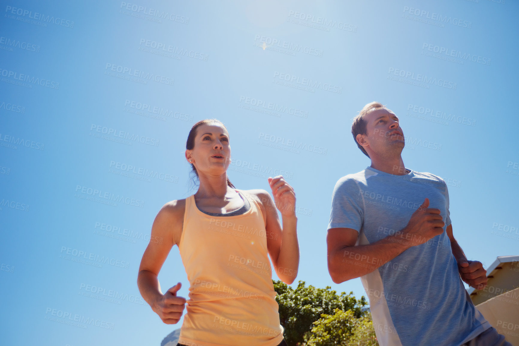 Buy stock photo Low angle shot of a happy couple jogging together in their neighborhood