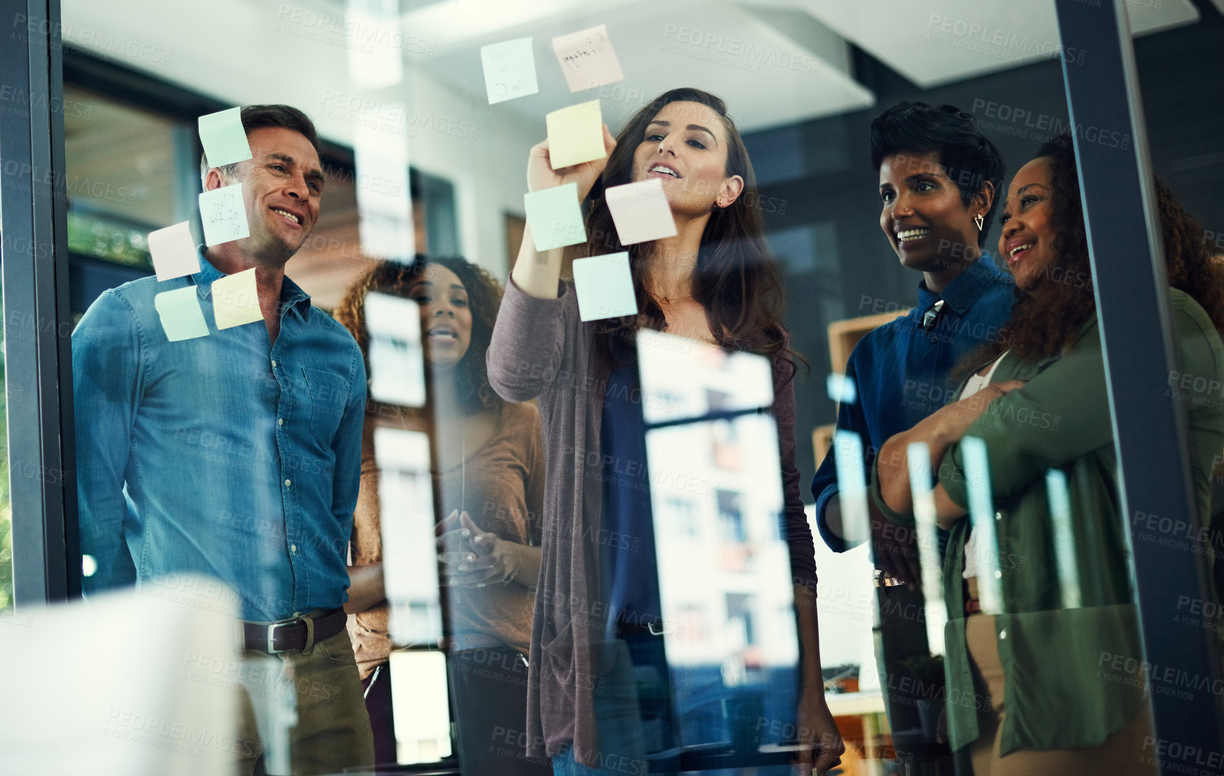 Buy stock photo Cropped shot of a group of businesspeople brainstorming with notes on a glass wall in an office