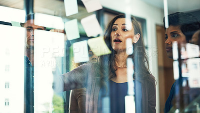 Buy stock photo Cropped shot of a group of businesspeople brainstorming with notes on a glass wall in an office