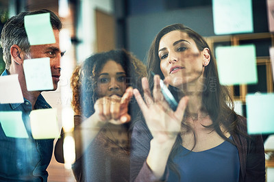 Buy stock photo Cropped shot of a group of businesspeople brainstorming with notes on a glass wall in an office