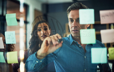 Buy stock photo Cropped shot of a group of businesspeople brainstorming with notes on a glass wall in an office