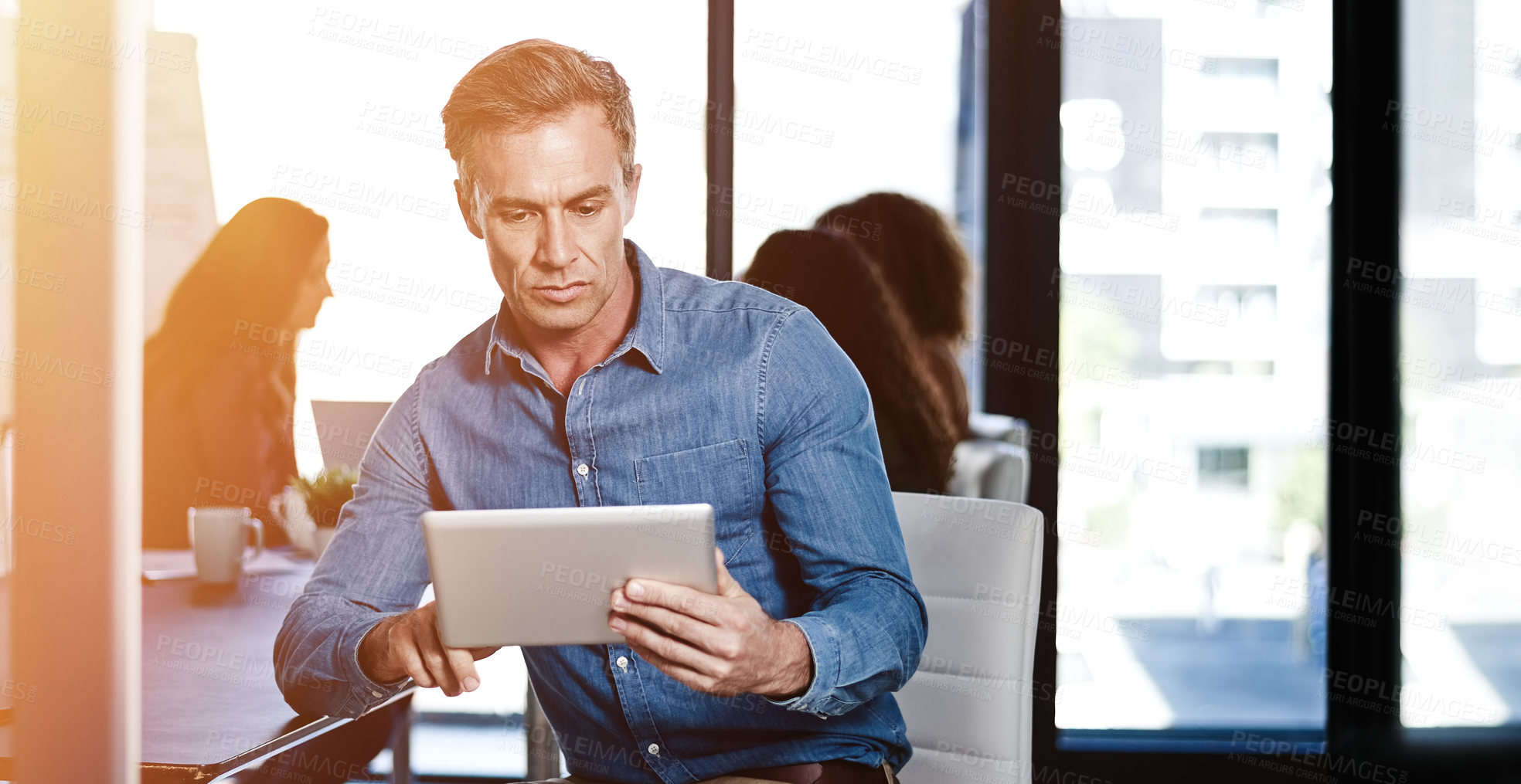 Buy stock photo Shot of a businessman using a digital tablet with his colleagues blurred in the background