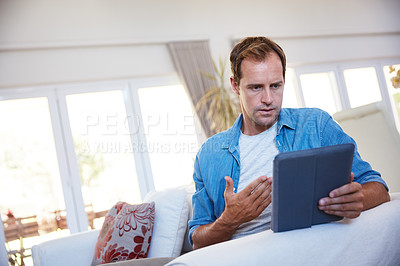 Buy stock photo Shot of a man looking frustrated while using a digital tablet at home