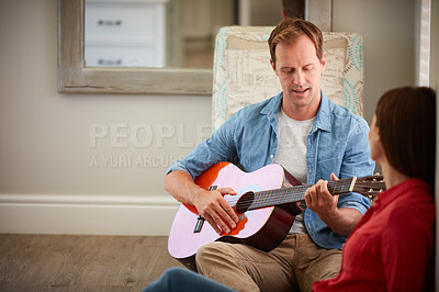 Buy stock photo Shot of a man playing the guitar for his wife at home