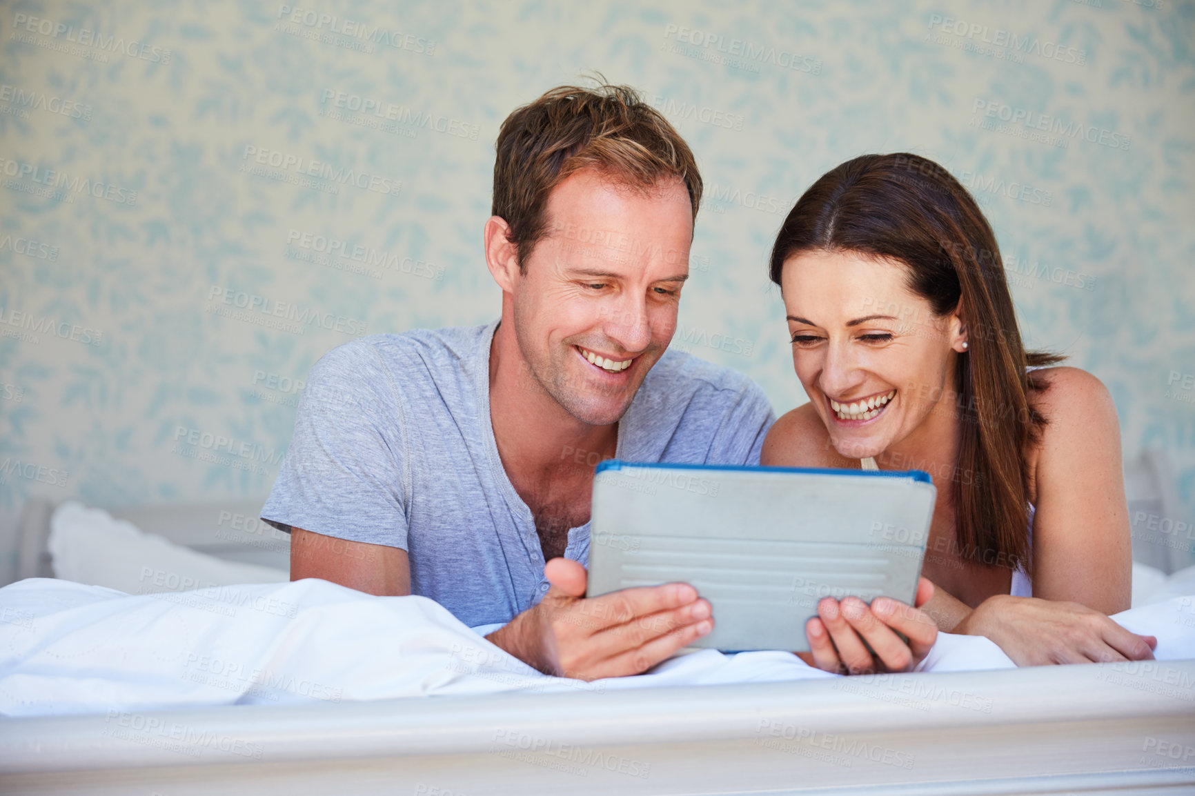 Buy stock photo Shot of a mature couple using a digital tablet while relaxing in bed together