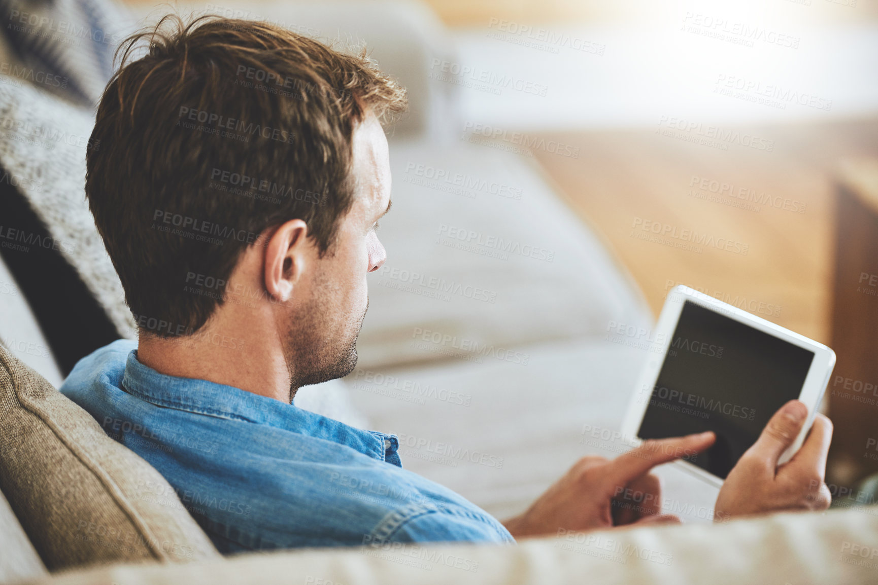 Buy stock photo High angle shot of a man using his tablet while sitting on the sofa at home