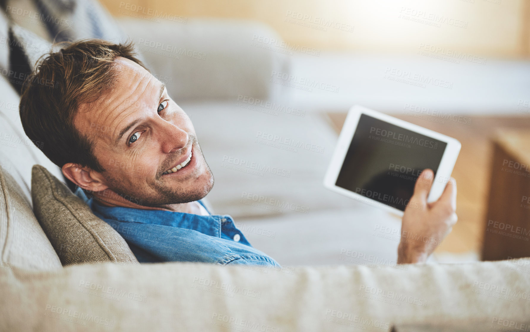 Buy stock photo High angle portrait of a man using his tablet while sitting on the sofa at home