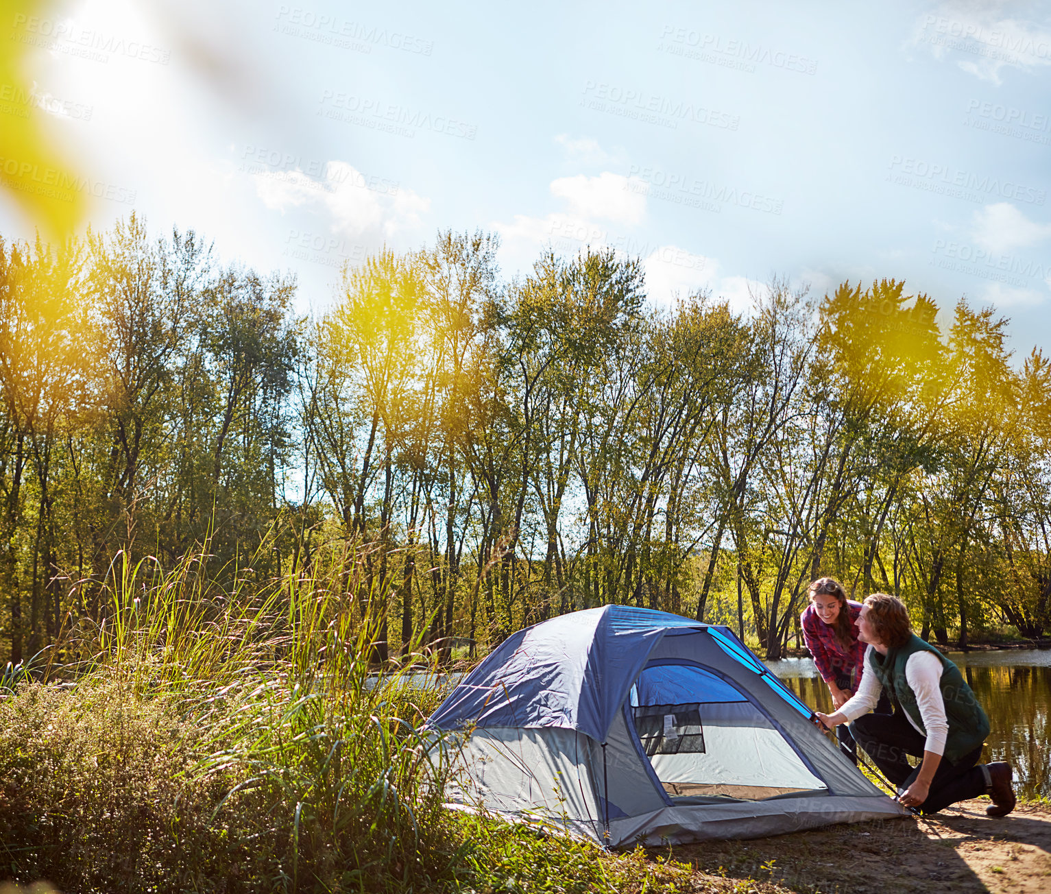 Buy stock photo Shot of an adventurous setting up their tent by the lake