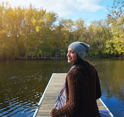 Buy stock photo Shot of a happy young woman standing on a pier next to a lake